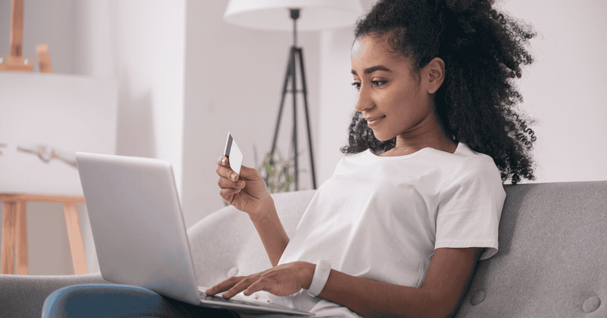 Mujer joven comprando online desde su laptop con una tarjeta de crédito, representando comodidad y compras digitales seguras.