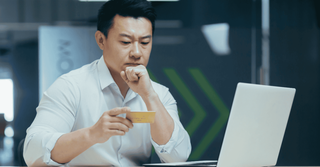 Hombre revisando los datos de su tarjeta de crédito frente a la computadora, analizando sus gastos y finanzas personales.