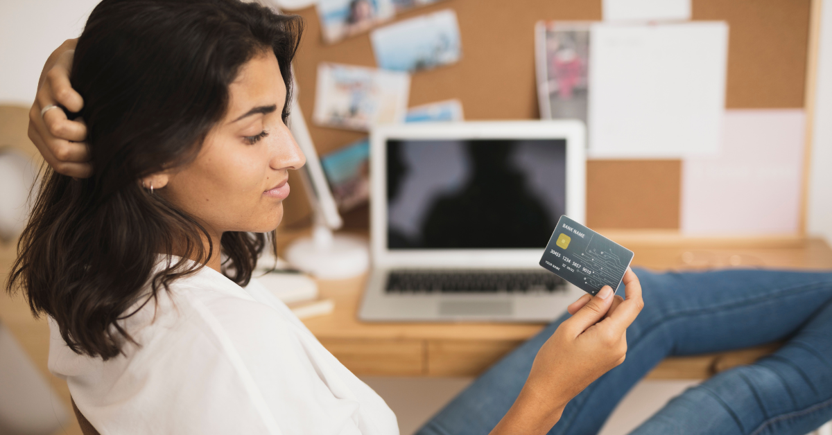 Mujer pensando frente a su computadora mientras observa una tarjeta de crédito, símbolo de control financiero y consumo responsable.