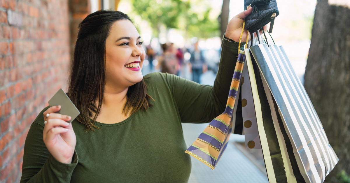 Mujer feliz con bolsas de compras y una tarjeta de crédito en la mano, representando consumo y bienestar financiero.