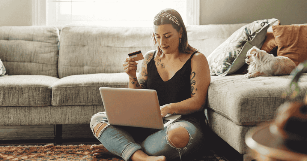 Mujer comprando por internet con su tarjeta de crédito mientras usa su computadora portátil en el living de su casa.