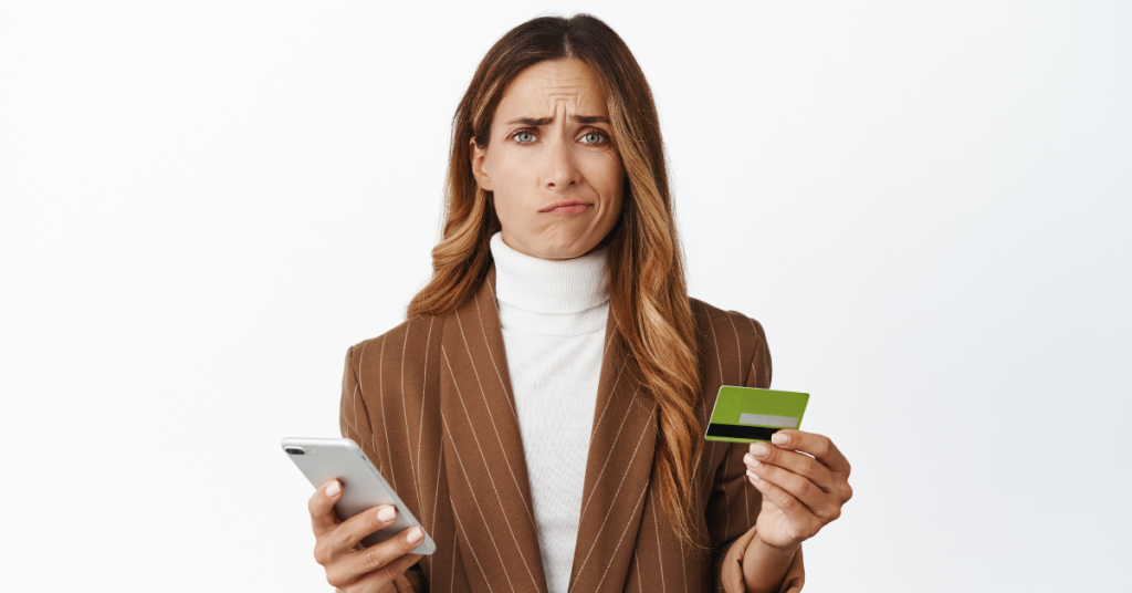 Mujer confundida sosteniendo una tarjeta de crédito y un teléfono, simbolizando problemas con pagos digitales.