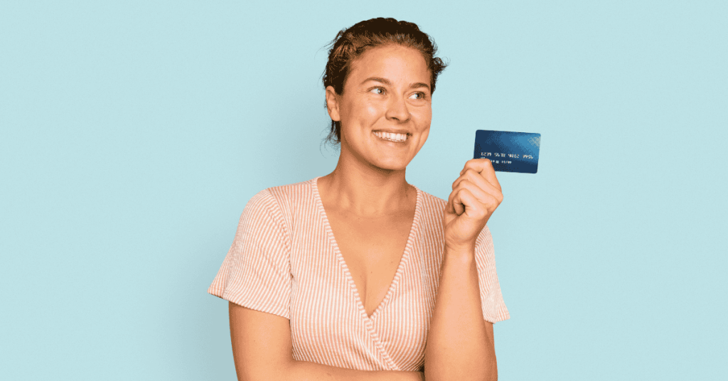 Mujer sonriendo mientras sostiene una tarjeta de crédito, símbolo de consumo e inversiones personales.