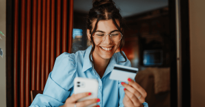 Mujer feliz utilizando su celular para hacer una compra online con tarjeta de crédito de forma segura.