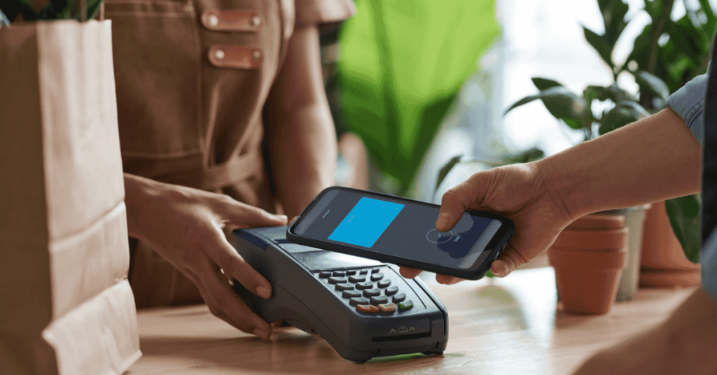 Cliente usando el celular para pagar con tarjeta de crédito contactless en un comercio, simbolizando pagos digitales rápidos y seguros.