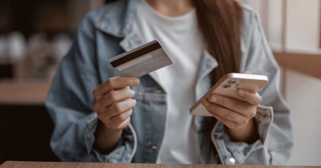 Persona sosteniendo una tarjeta de crédito y un teléfono móvil para realizar un pago online de forma segura.
