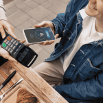 Pago con celular y terminal electrónica en un restaurante, vinculado a las finanzas digitales.