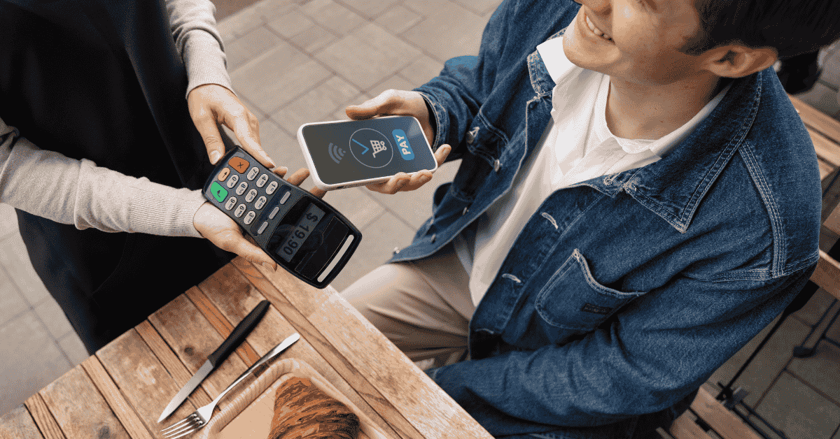 Pago con celular y terminal electrónica en un restaurante, vinculado a las finanzas digitales.